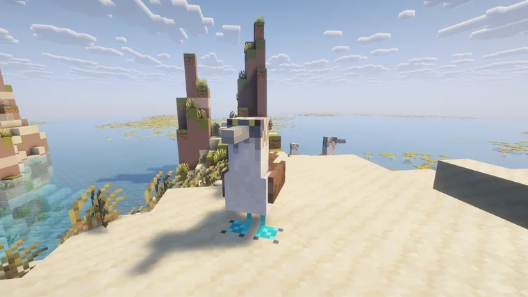 A tall white wading bird on a sandy shore beside turquoise water and sandstone cliffs.