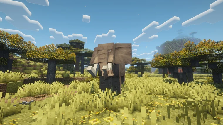 A large elephant standing in golden savanna grass among flat-topped trees.