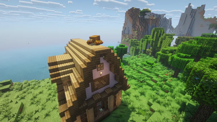 A tall wooden house with a spiral shingled roof, on a grassy cliff overlooking the sea.